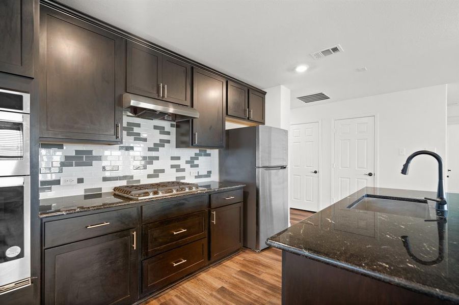 Kitchen with light wood-type flooring, dark stone counters, dark brown cabinets, sink, and stainless steel appliances