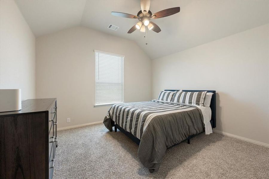 This upstairs secondary bedroom features light carpet, lofted ceiling, and ceiling fan