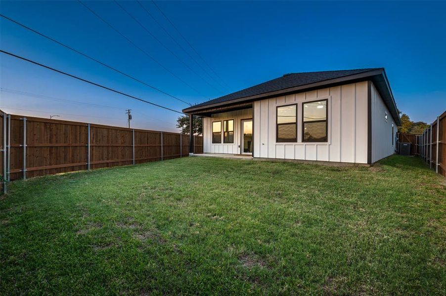 Rear view of property featuring central AC unit and a lawn