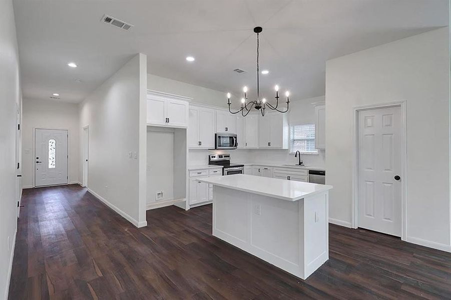 Kitchen with dark hardwood / wood-style floors, a center island, decorative light fixtures, white cabinetry, and appliances with stainless steel finishes