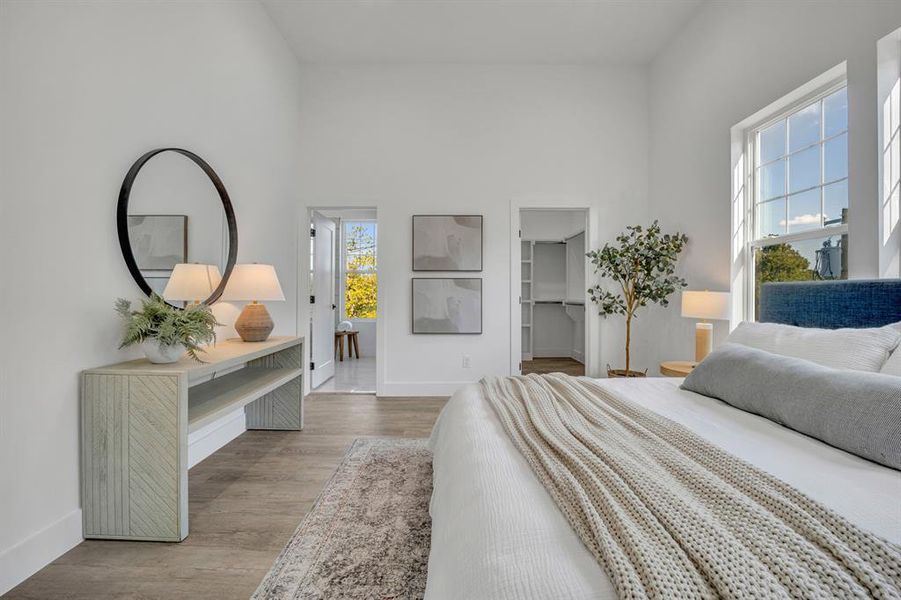 Bedroom with light wood-type flooring, a towering ceiling, multiple windows, and a walk in closet