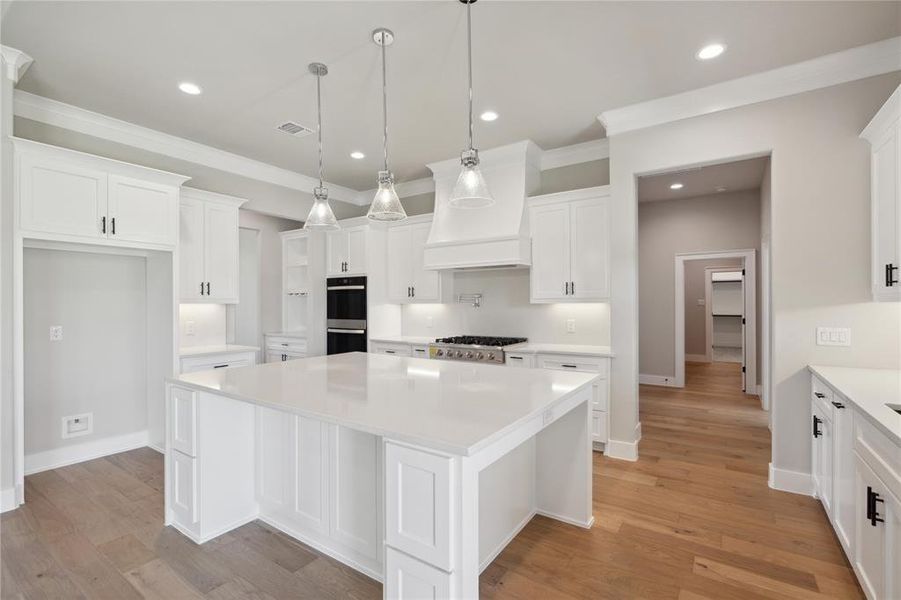 Kitchen with stainless steel appliances, a kitchen island, hanging light fixtures, light hardwood / wood-style floors, and white cabinets