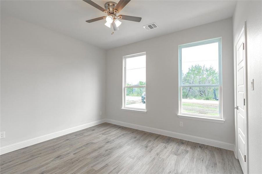 Empty room with light wood-type flooring, ceiling fan, and a healthy amount of sunlight