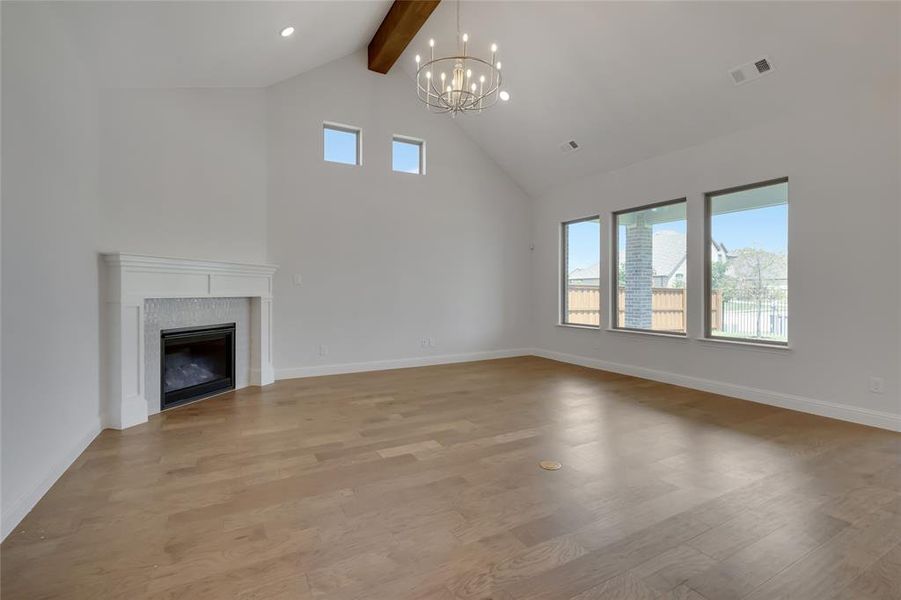 Unfurnished living room with light hardwood / wood-style flooring, high vaulted ceiling, an inviting chandelier, and beam ceiling