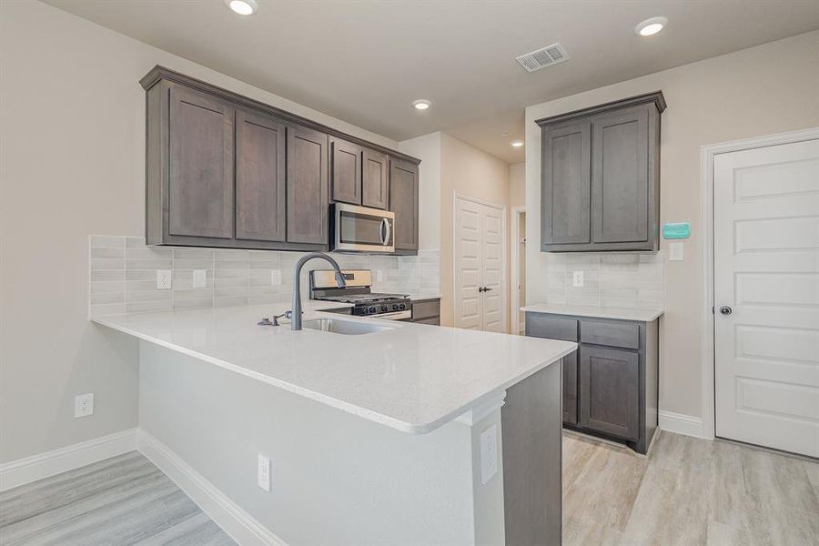 Kitchen featuring light hardwood / wood-style floors, tasteful backsplash, appliances with stainless steel finishes, and kitchen peninsula