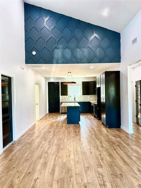 Kitchen featuring tasteful backsplash, black fridge, a kitchen bar, a towering ceiling, and light hardwood / wood-style floors