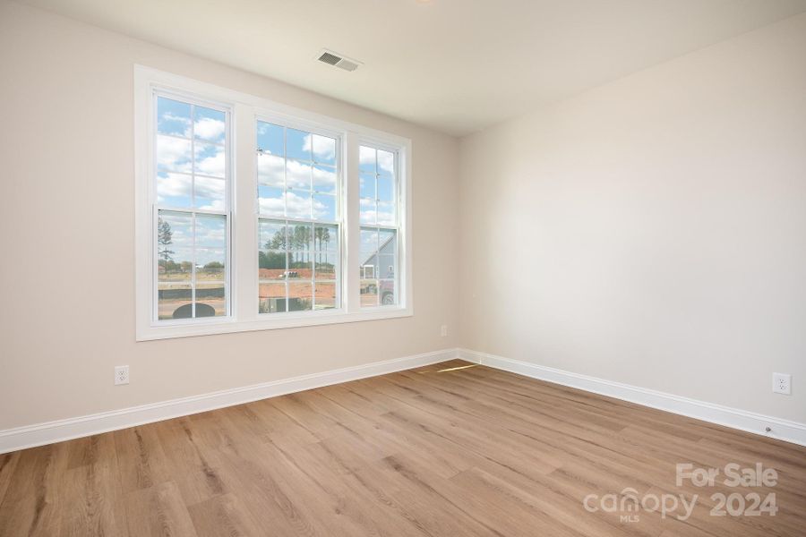 Secondary Bedroom at the front of the home offers great natural light, upgraded LVP flooring, neutral paint and privacy from the Primary Suite.
