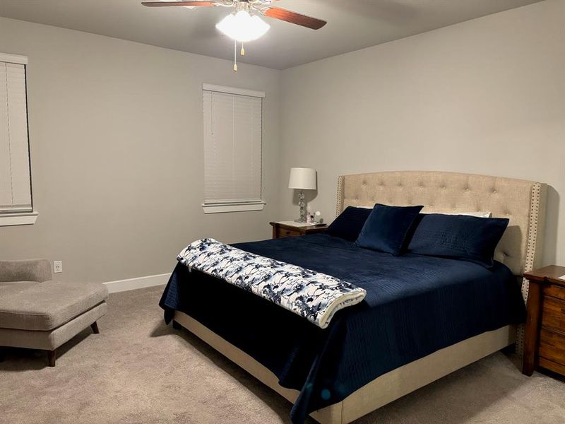 This is a cozy, neutrally decorated  and two windows providing natural light. It features plush carpeting and a ceiling fan for added comfort.