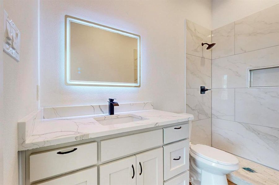 Bathroom with tiled shower, oversized vanity, and toilet