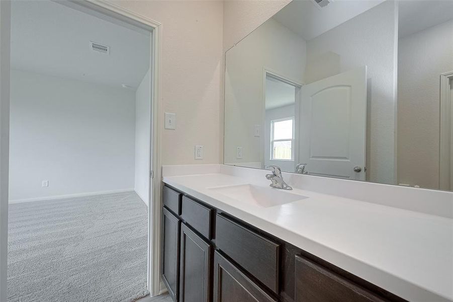 Modern bathroom with double sink vanity, large mirror, and a view into a carpeted room through an open door.