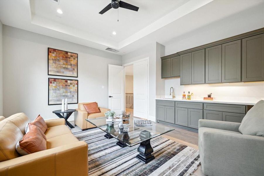 This photo shows a modern, open-concept living space with a comfortable sitting area and a sleek kitchenette with ample cabinetry. The room features neutral tones, contemporary furniture, and a touch of color from decorative pillows and wall art.