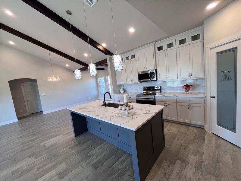 Kitchen with sink, an island with sink, white cabinets, hanging light fixtures, and stainless steel appliances