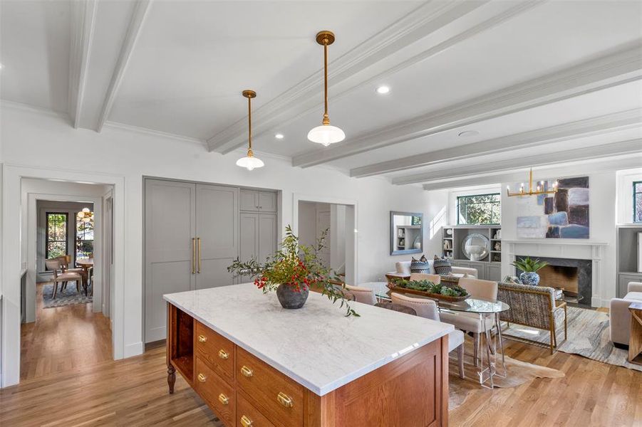 Kitchen featuring a fireplace, light wood-type flooring, beamed ceiling, gray cabinets, and decorative light fixtures