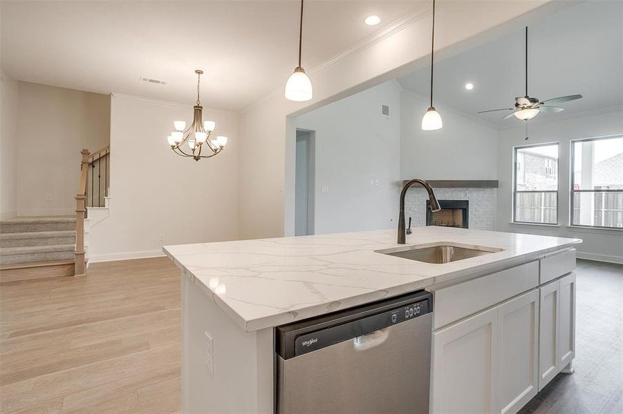 Kitchen with stainless steel dishwasher, pendant lighting, sink, light hardwood / wood-style floors, and a brick fireplace