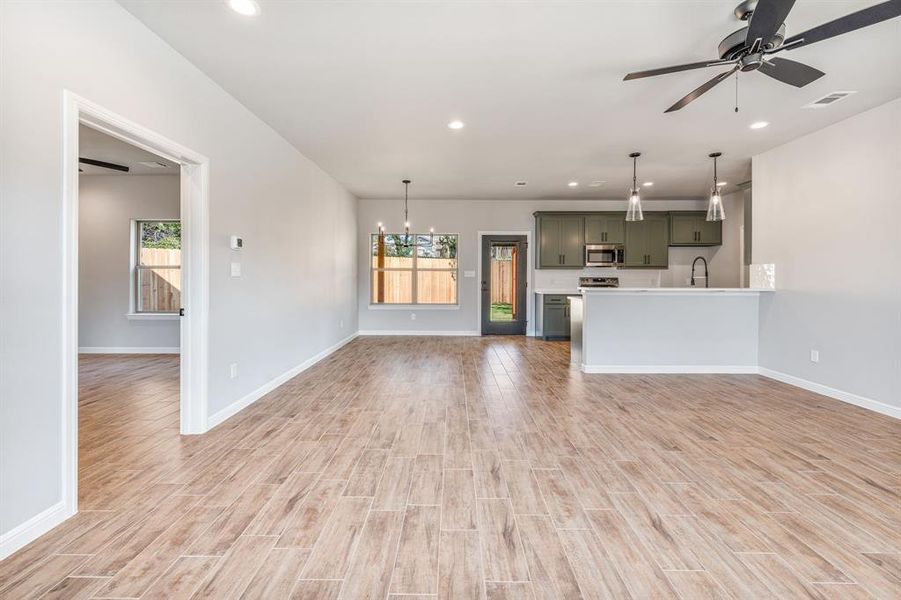 Unfurnished living room featuring ceiling fan with notable chandelier, light hardwood / wood-style floors, sink, and a wealth of natural light