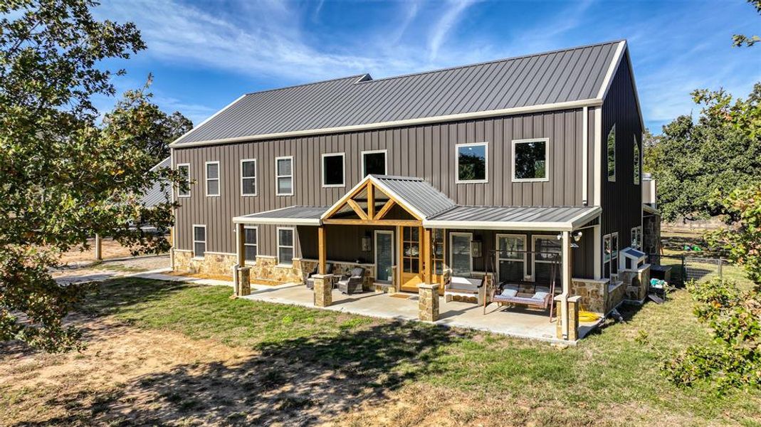 A spacious front porch offers a serene view of lush trees and sprawling pastures, inviting relaxation and connection with nature.