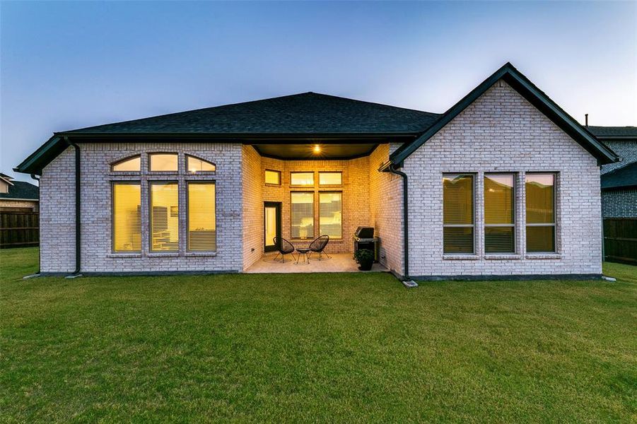 Back house at dusk with a patio area and a lawn