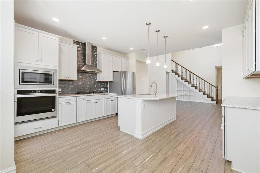 Kitchen with white cabinets, appliances with stainless steel finishes, light wood-type flooring, and wall chimney exhaust hood