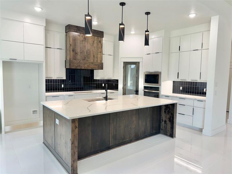 Kitchen featuring stainless steel appliances, backsplash, a center island with sink, sink, and decorative light fixtures