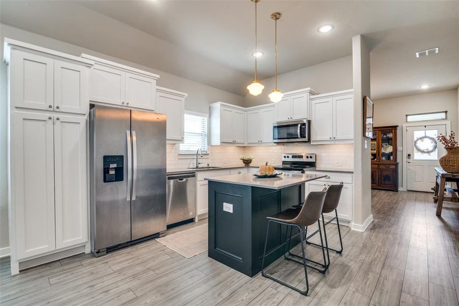 Kitchen featuring appliances with stainless steel finishes, light hardwood / wood-style floors, white cabinets, a center island, and decorative light fixtures