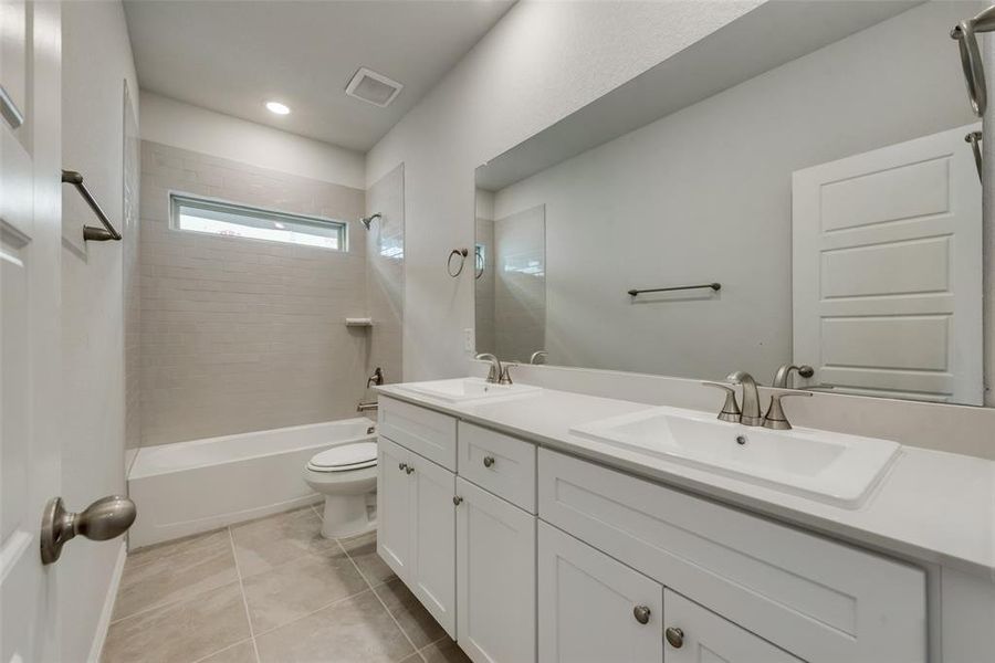 Full bathroom with dual vanity, tiled shower / bath combo, toilet, and tile patterned floors