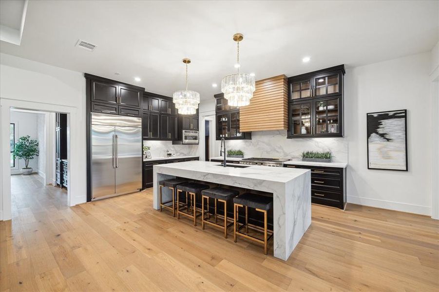 A custom reeded wood vent hood sits between upper cabinets with glass inserts. Pendant lighting highlights the elegance of this kitchen.