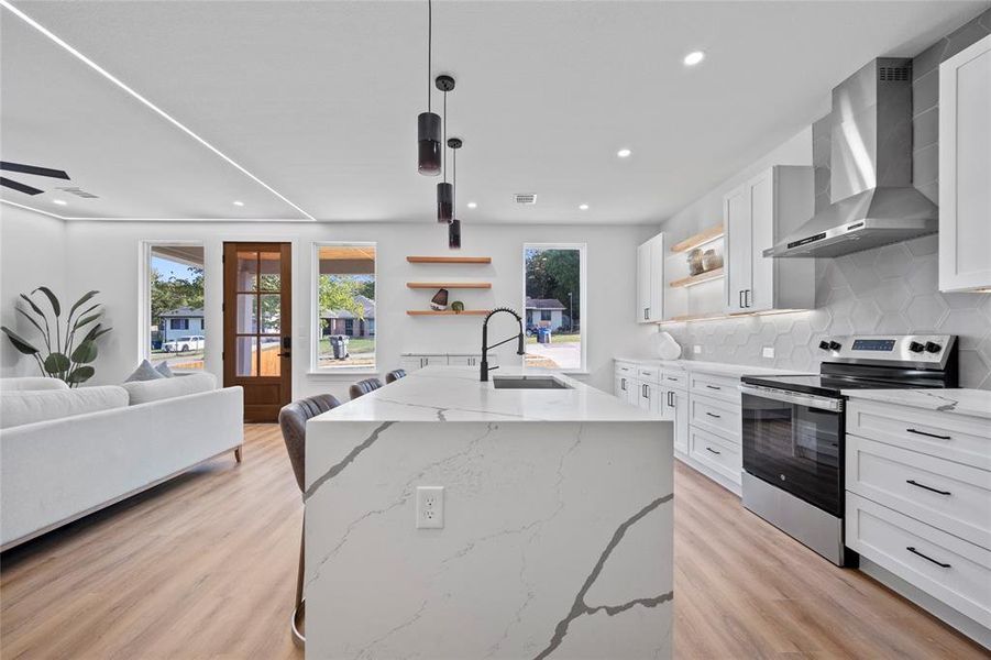 Kitchen featuring pendant lighting, an island with sink, wall chimney exhaust hood, white cabinetry, and stainless steel range with electric cooktop