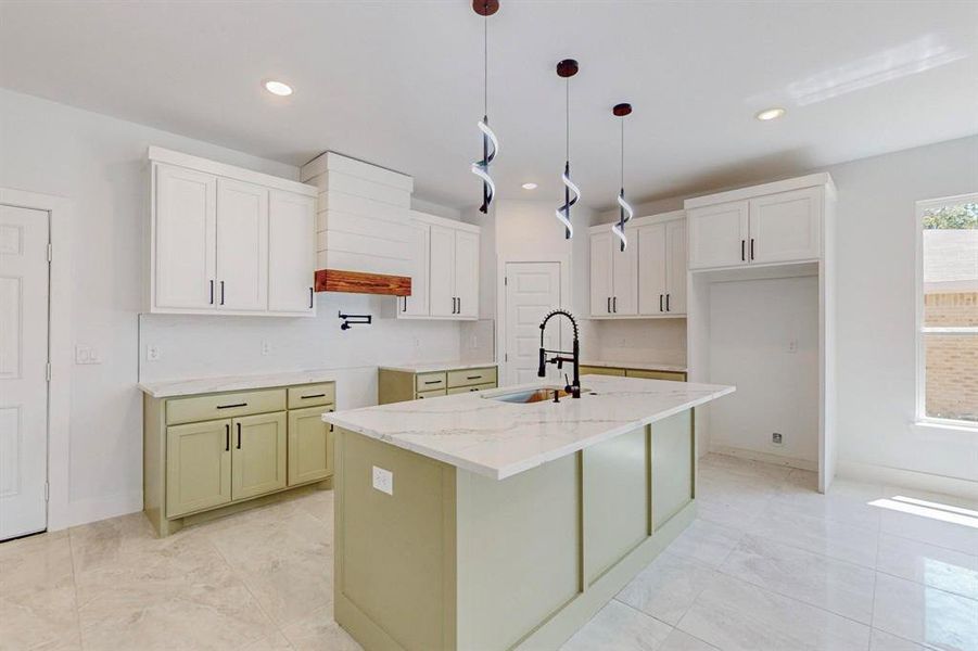 Kitchen featuring white cabinetry, light tile patterned floors, hanging light fixtures, sink, and a center island with sink