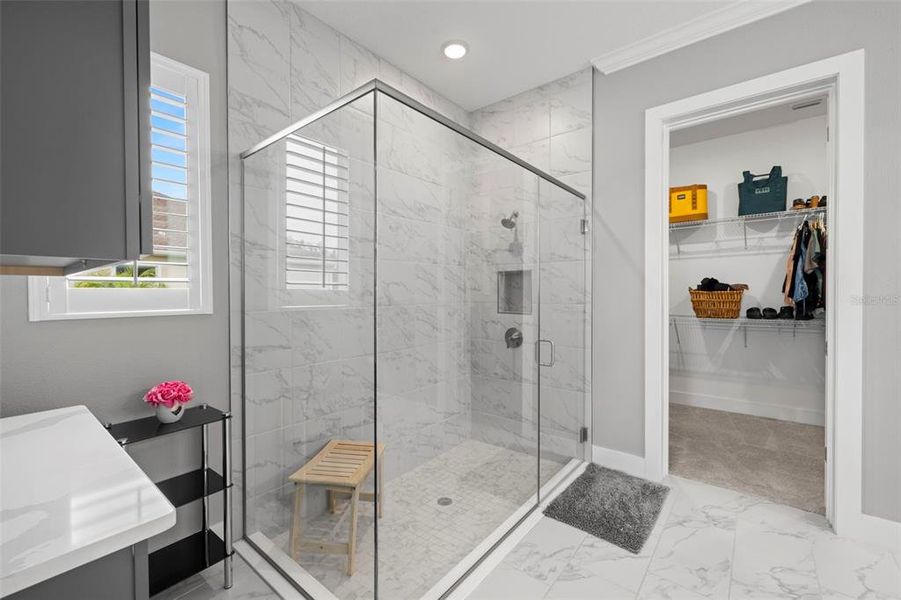 Primary En-Suite Bath Includes a Sizable Tiled Shower with Frameless Glass Doors & Storage Nook