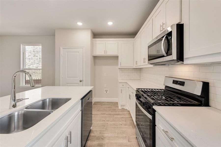 Kitchen with stainless steel appliances, white cabinets, light hardwood / wood-style floors, and sink