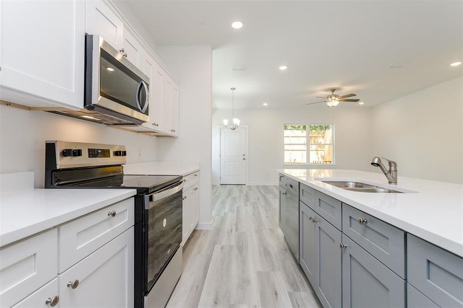 Kitchen with ceiling fan, light hardwood / wood-style floors, stainless steel appliances, sink, and white cabinetry