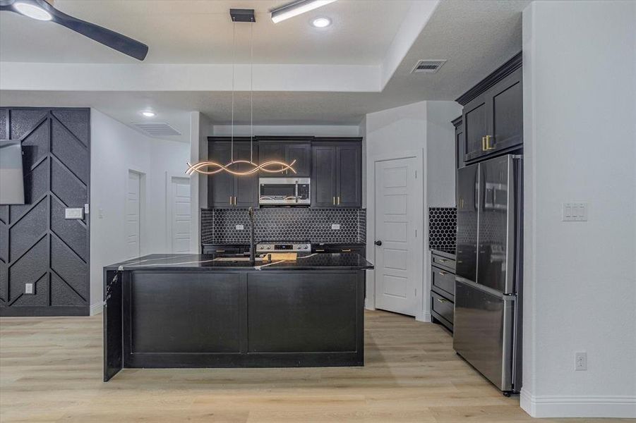 Kitchen with decorative light fixtures, light hardwood / wood-style floors, backsplash, and stainless steel appliances