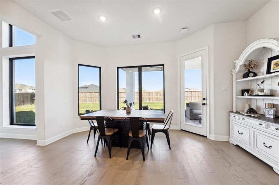 The dining space is right off of the kitchen and features large windows, elegant light wood flooring, and a sophisticated built-in white cabinetry unit.