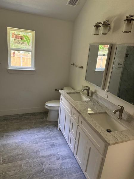 Angle view of the Master Bathroom featuring double vanity, tile patterned floors, toilet, and a wealth of natural light from the windows