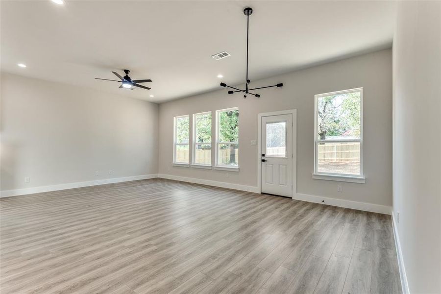 Unfurnished living room with light wood-type flooring and ceiling fan with notable chandelier