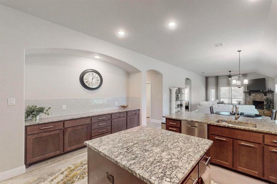 Kitchen featuring stainless steel dishwasher, a fireplace, sink, a center island, and vaulted ceiling