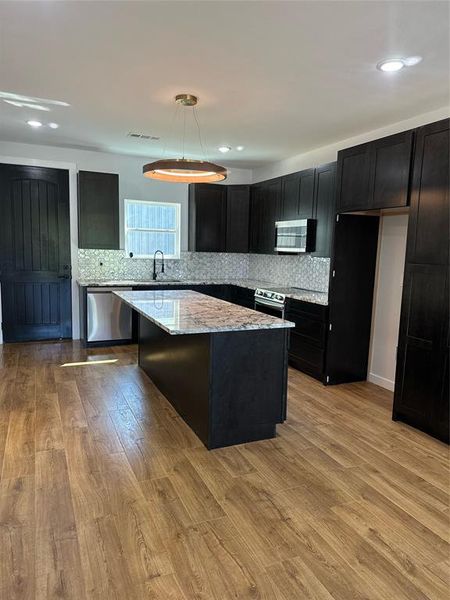 Kitchen with a kitchen island, dishwashing machine, light wood-type flooring, decorative light fixtures, and light stone counters