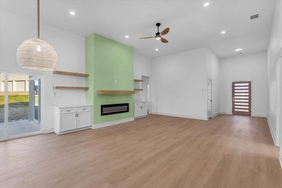 Unfurnished living room with light hardwood / wood-style floors, ceiling fan, and a high ceiling