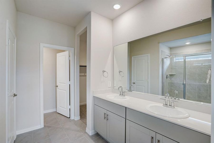 Tiled shower with glass door, tile patterned floors, and double vanity