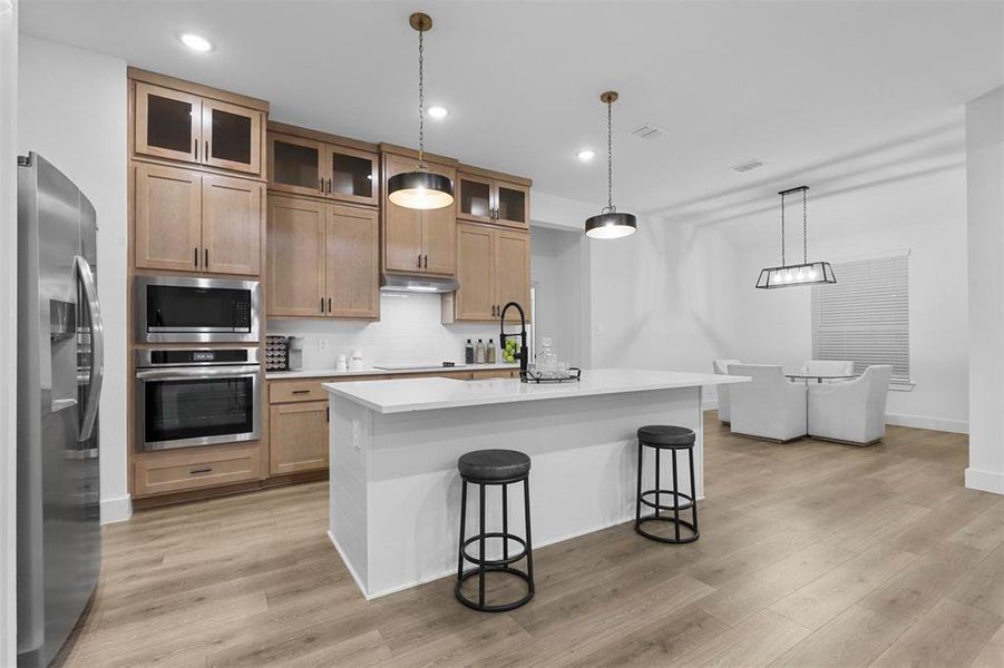 Kitchen featuring stainless steel appliances, light hardwood / wood-style floors, a center island with sink, and pendant lighting