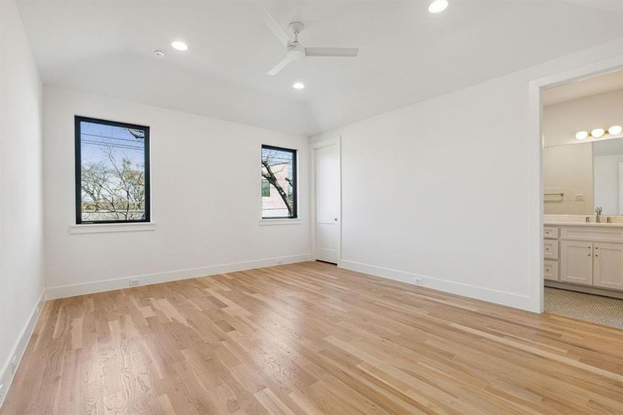 Unfurnished bedroom featuring ceiling fan, lofted ceiling, sink, ensuite bath, and light hardwood / wood-style floors