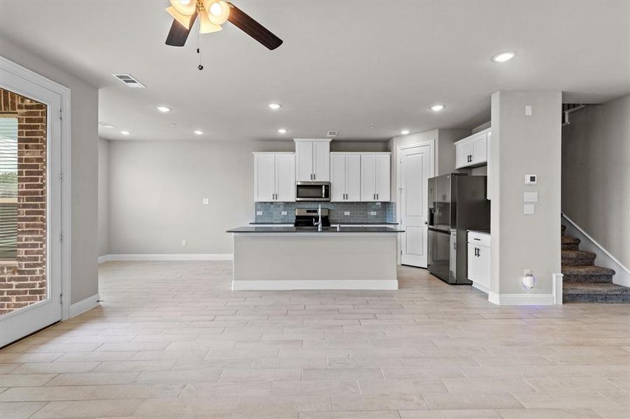 Kitchen featuring white cabinets, appliances with stainless steel finishes, ceiling fan, decorative backsplash, and a center island with sink