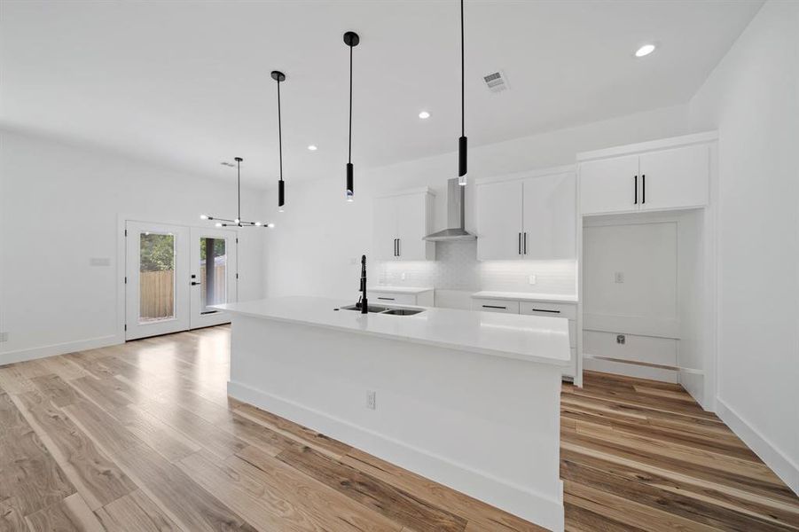 Kitchen with white cabinets, decorative light fixtures, light wood-type flooring, and a kitchen island with sink