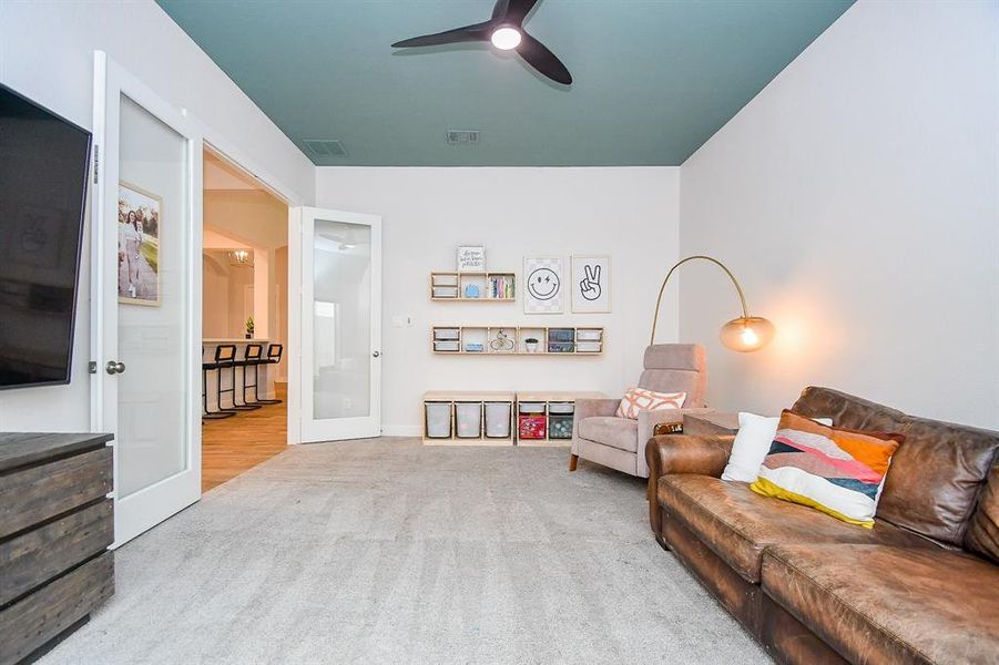 Spacious, well-lit game room featuring a vaulted ceiling with a contrasting paint accent, large windows providing ample natural light, double doors with glass accent. New carpet creates a clean, inviting space. a ceiling fan.