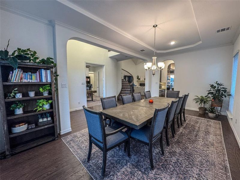 Dining space with a raised ceiling, ornamental molding, dark hardwood / wood-style flooring, and a chandelier