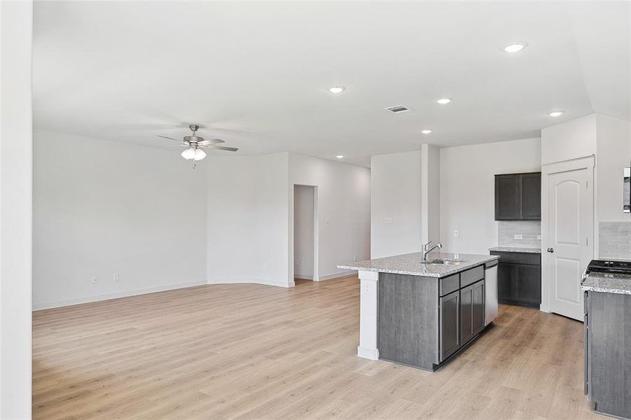 Kitchen featuring light hardwood / wood-style floors, tasteful backsplash, sink, light stone countertops, and an island with sink