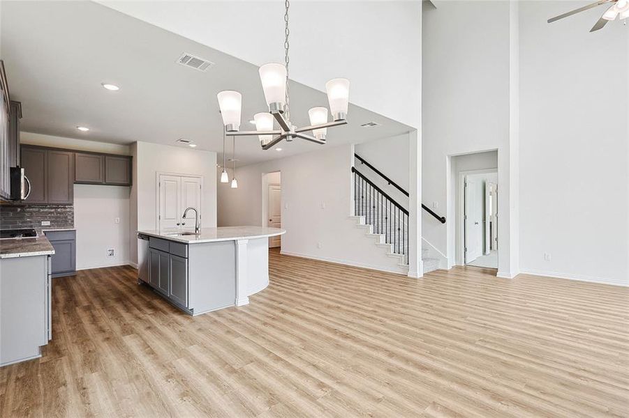 Kitchen with light hardwood / wood-style floors, tasteful backsplash, ceiling fan with notable chandelier, hanging light fixtures, and a kitchen island with sink