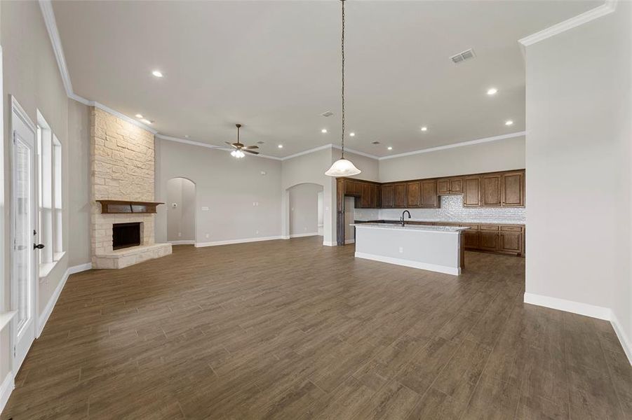 Unfurnished living room with dark wood-type flooring, sink, crown molding, a fireplace, and ceiling fan