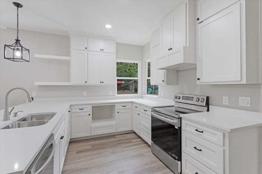 Kitchen featuring decorative light fixtures, appliances with stainless steel finishes, sink, light wood-type flooring, and white cabinets