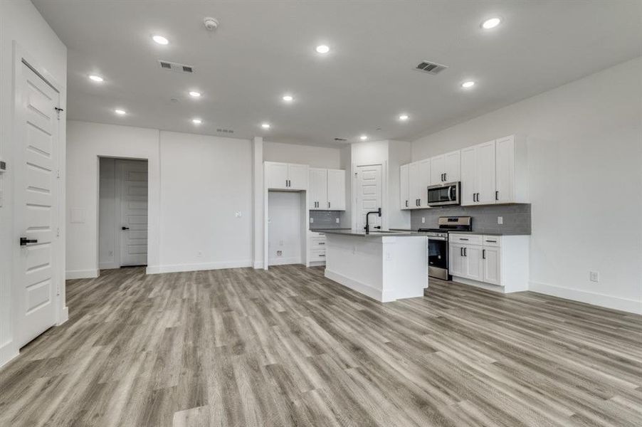 Kitchen with white cabinetry, appliances with stainless steel finishes, an island with sink, and light wood-type flooring